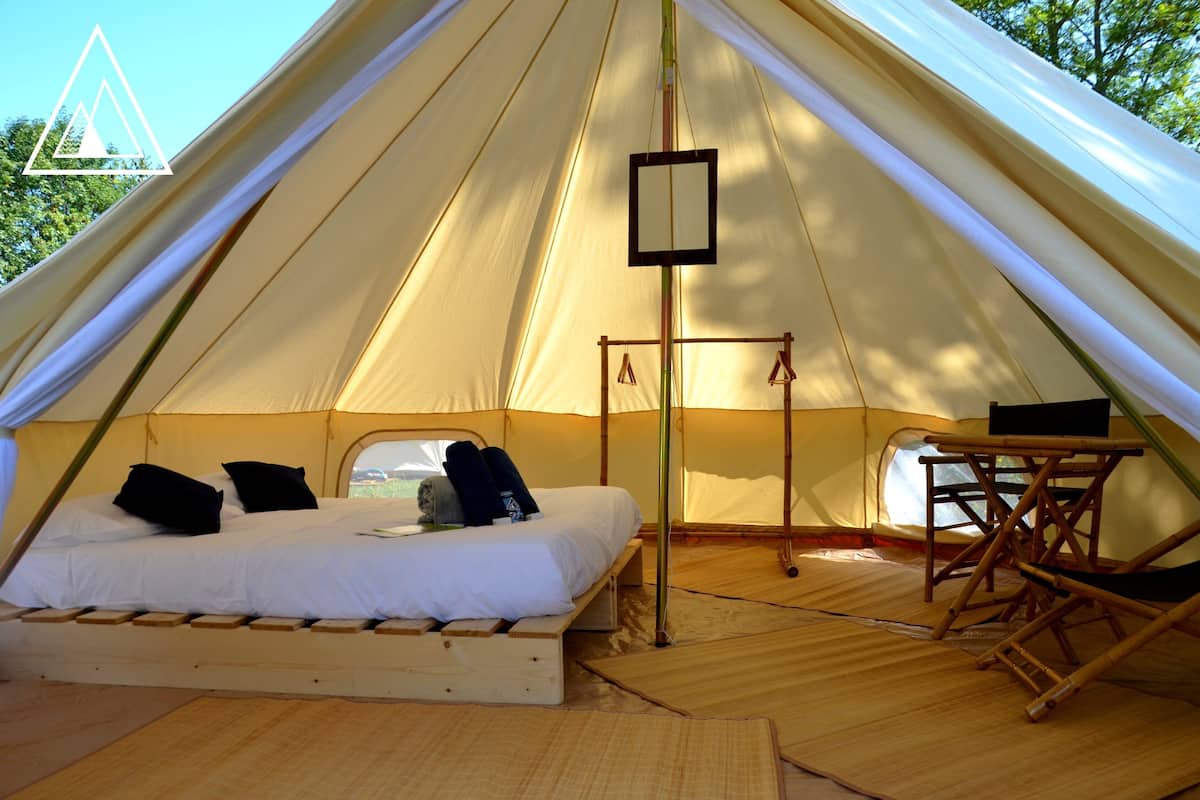 A tent with a bed, a small table, and a hanging light fixture.