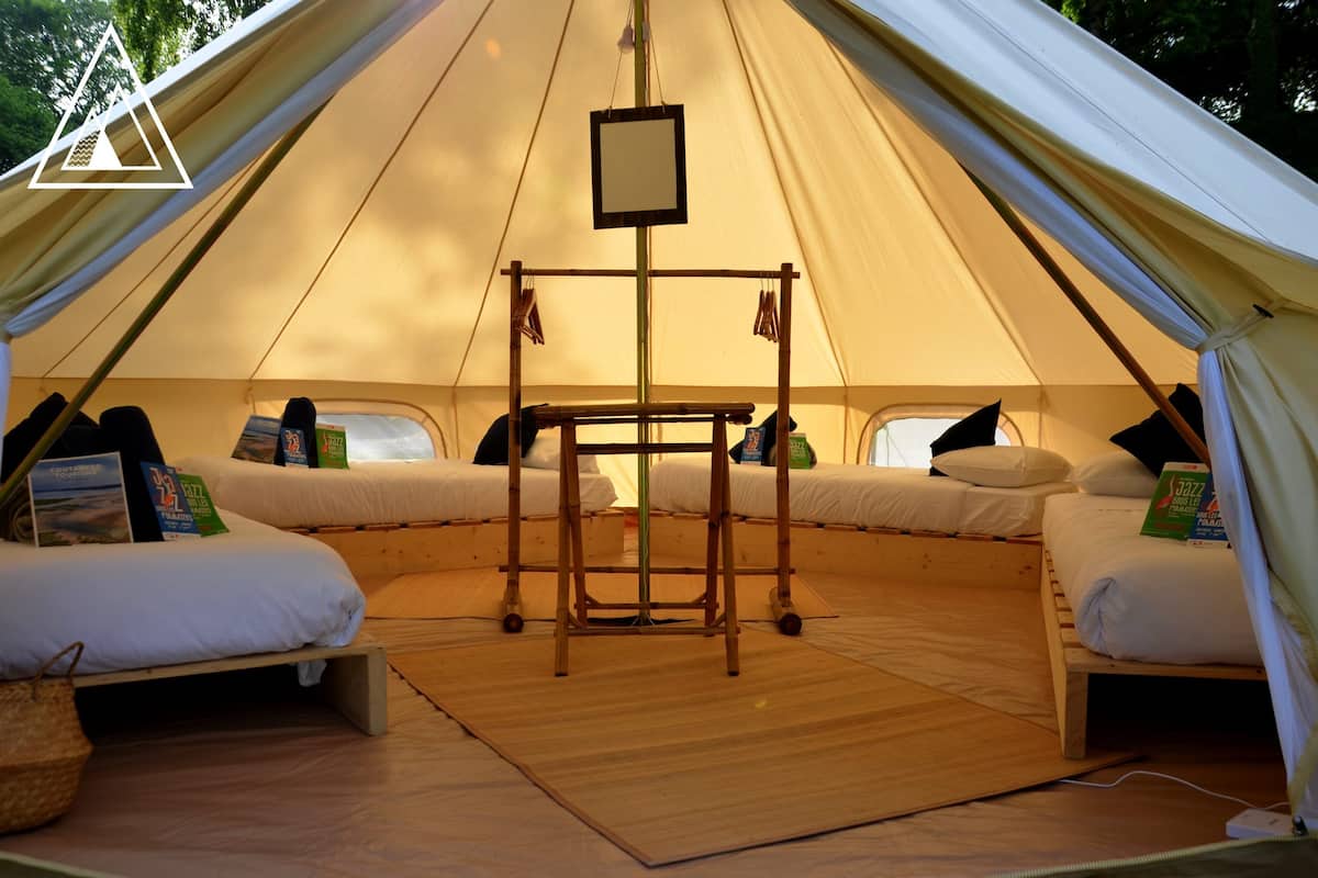 A tent with two beds, a central table, and a hanging light fixture.
