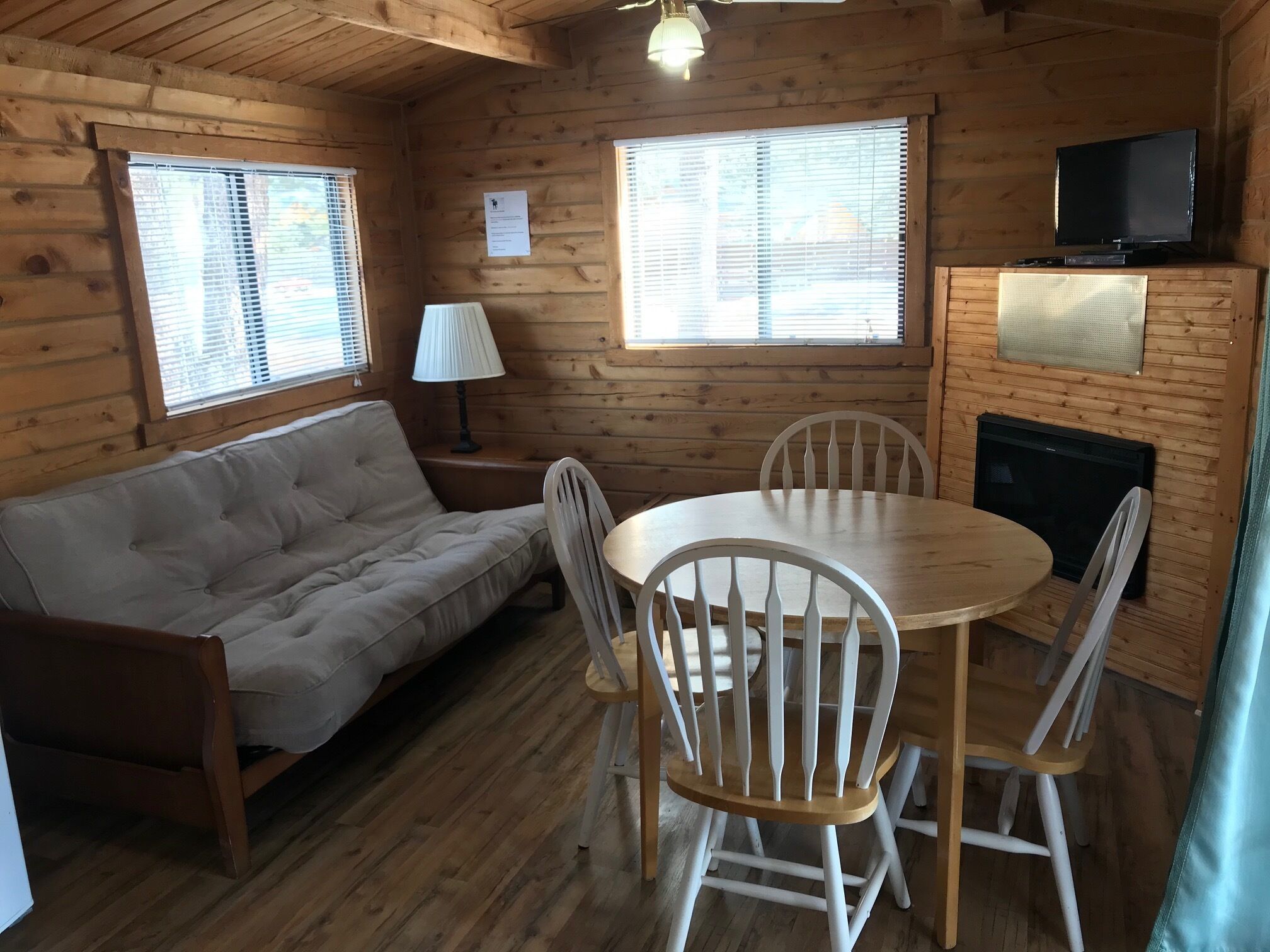Een gezellig interieur van een chalet met een bank, eettafel, stoelen, een lamp, een televisie en een open haard.