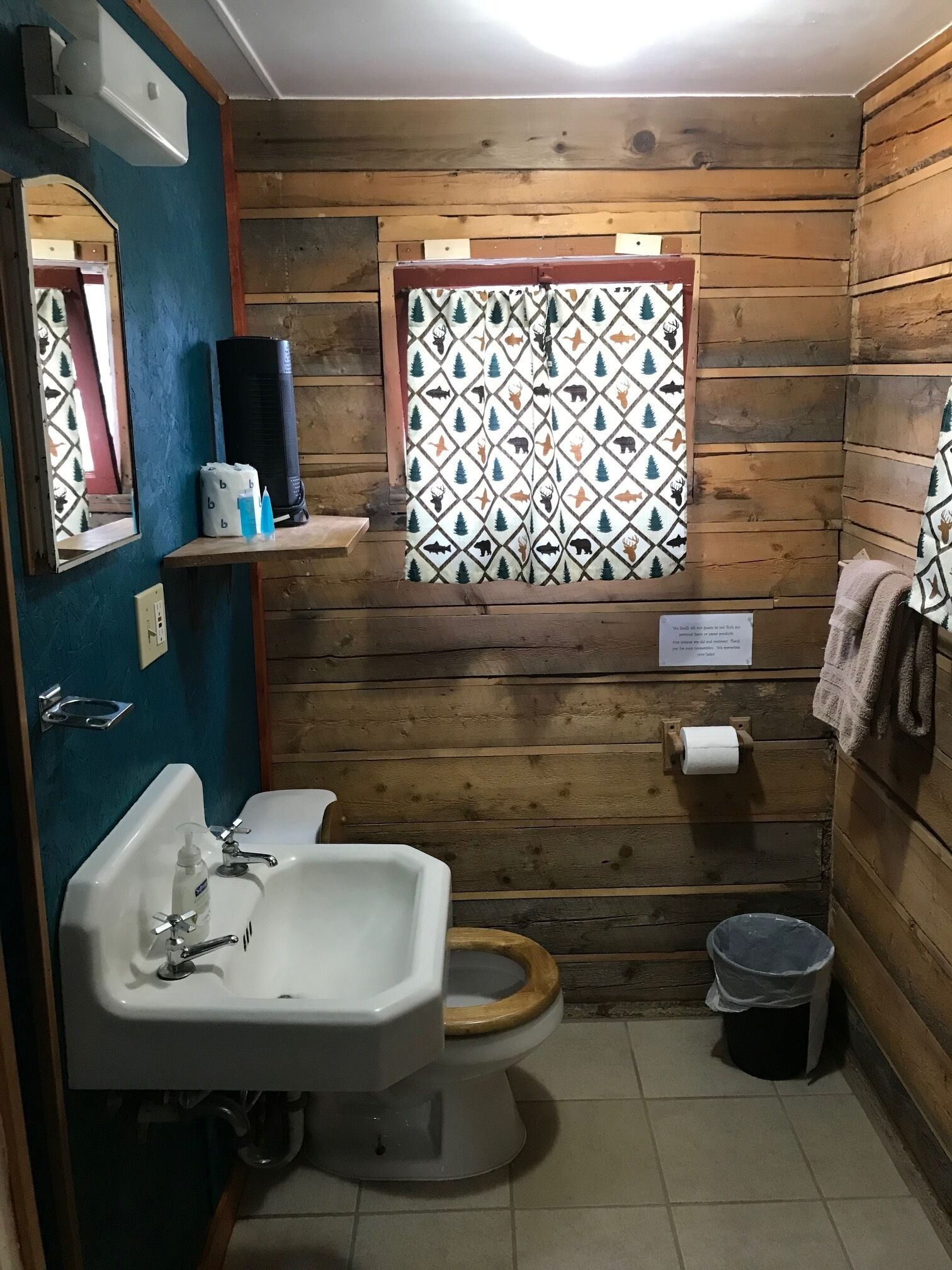 Een klein houten badkamertje met een wastafel, toilet en een raam met een geometrisch patroon.