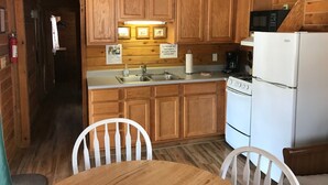A wooden cabin-style kitchen with a sink, stove, refrigerator, and microwave.