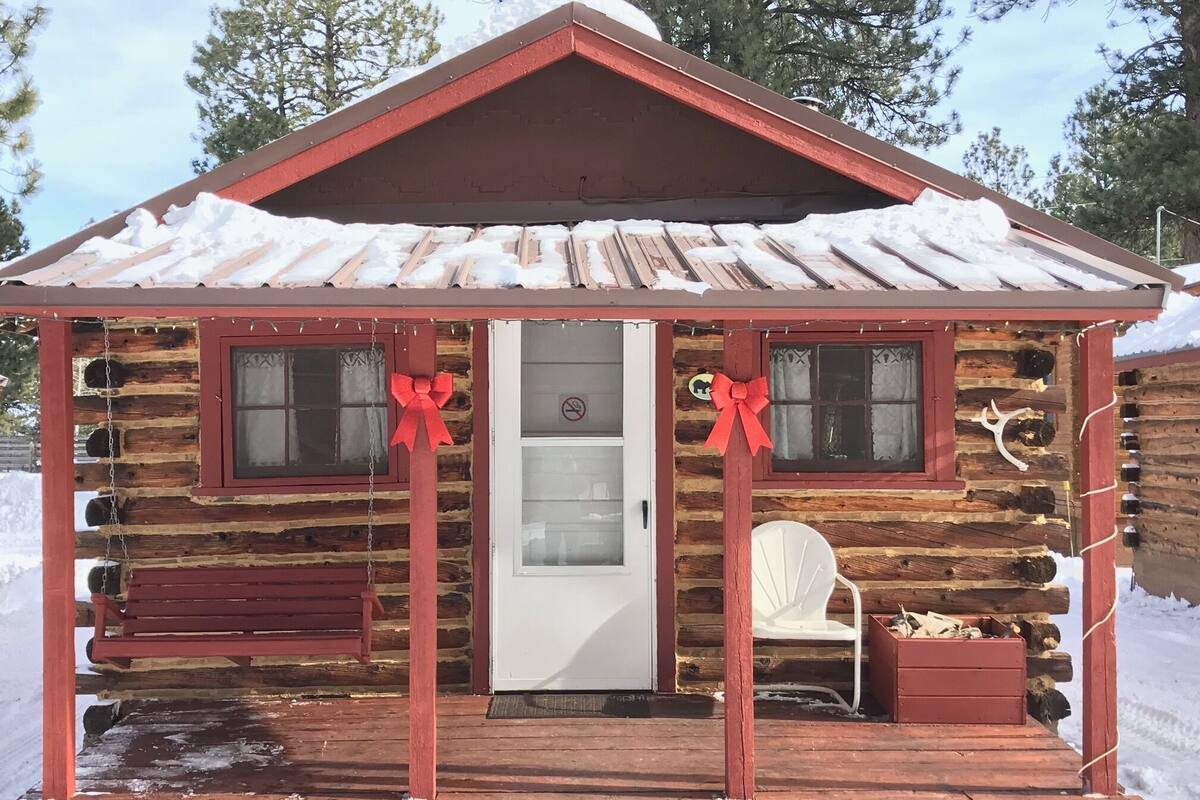 A log cabin with a porch, a white door, and two windows adorned with red bows.