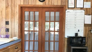 A wooden-paneled room with a double door, a whiteboard with a schedule, a microwave, and a fire extinguisher.