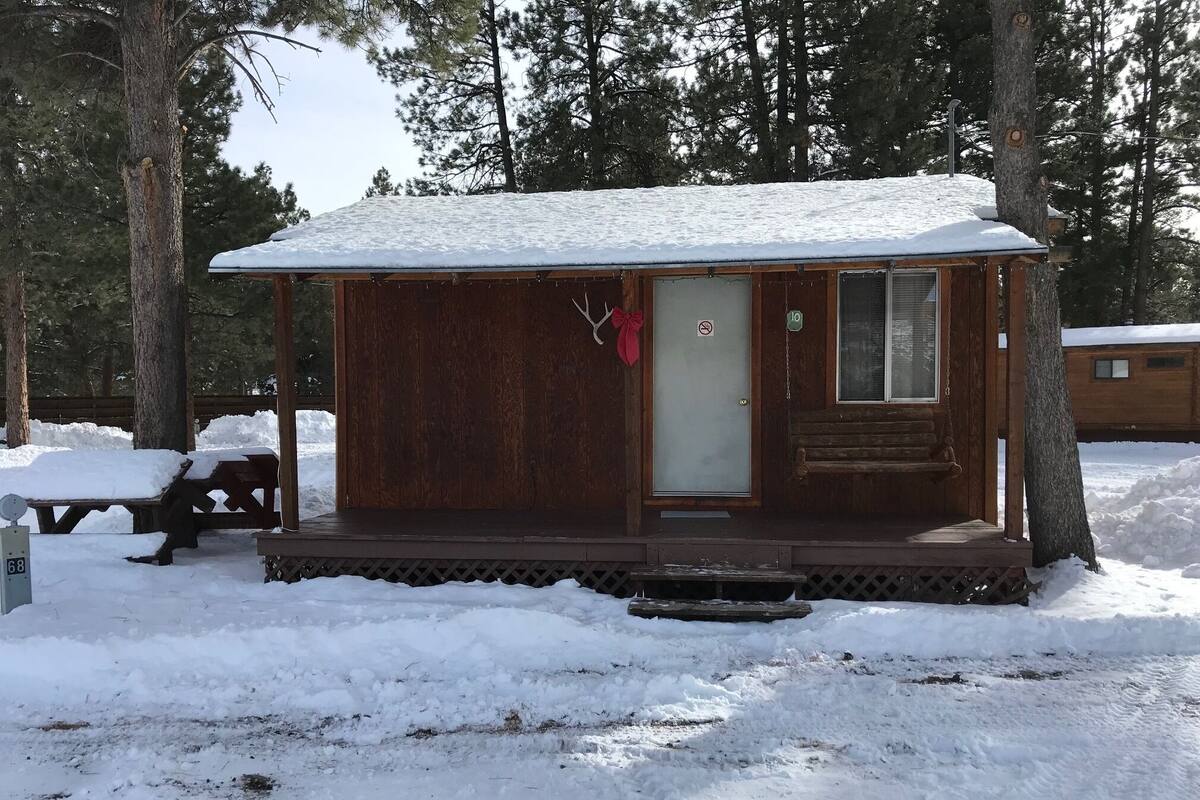 A wooden cabin with a snow-covered roof, a front door, and a small porch area.