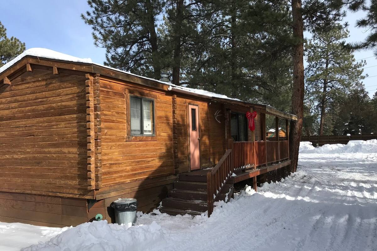 A wooden cabin with a porch, surrounded by snow and trees.