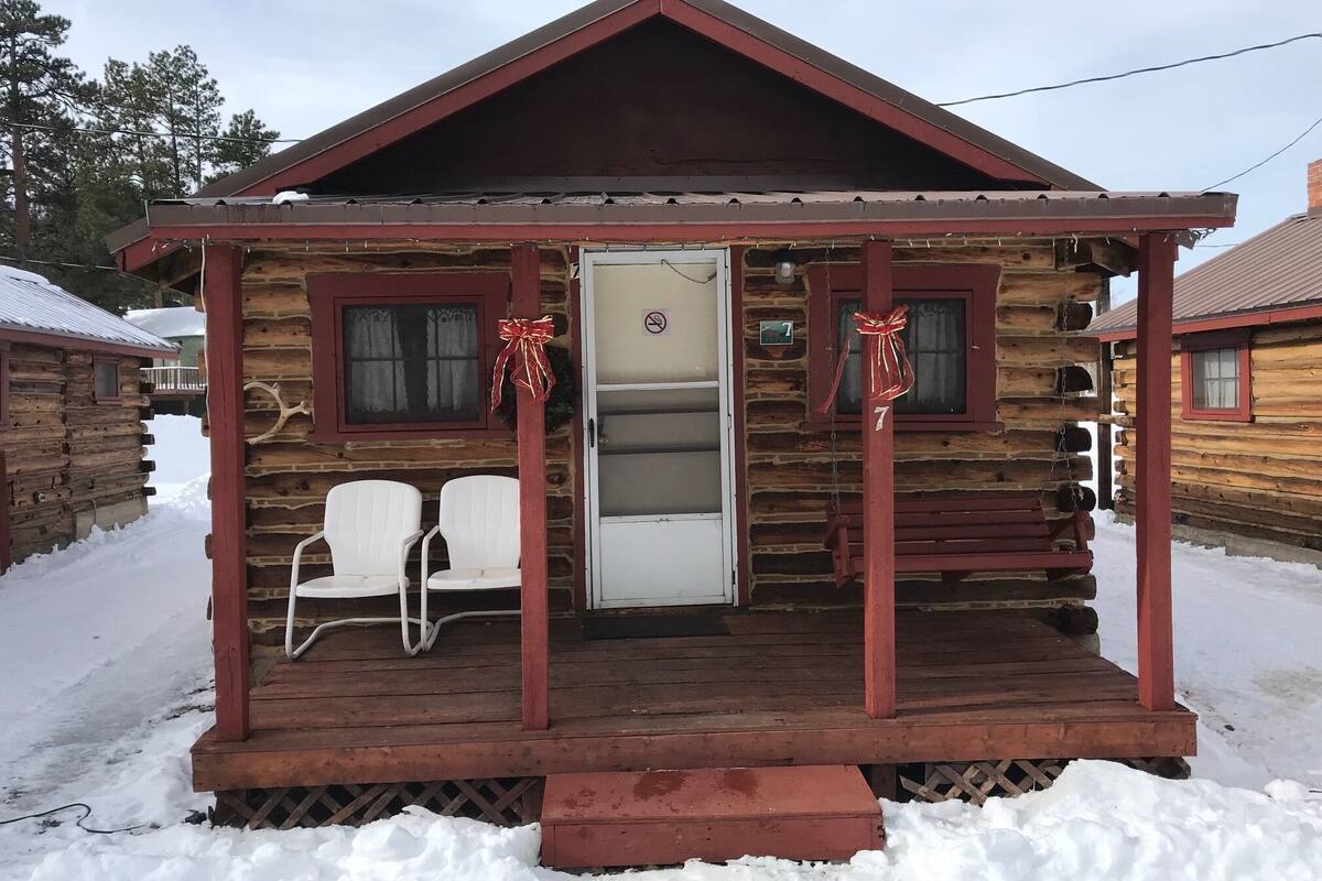 A log cabin with a wooden porch, two white chairs, and a bench.