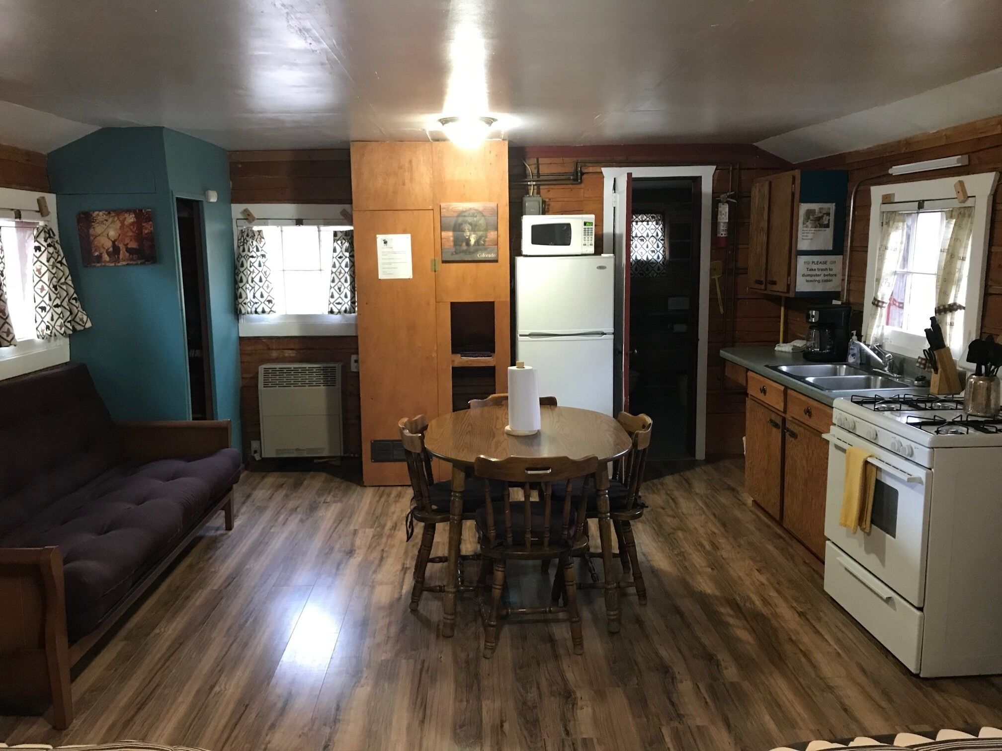 A compact kitchen with wooden cabinets, a dining table with chairs, a refrigerator, a microwave, and a stove.