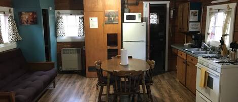 A compact kitchen with wooden cabinets, a dining table with chairs, a refrigerator, a microwave, and a stove.