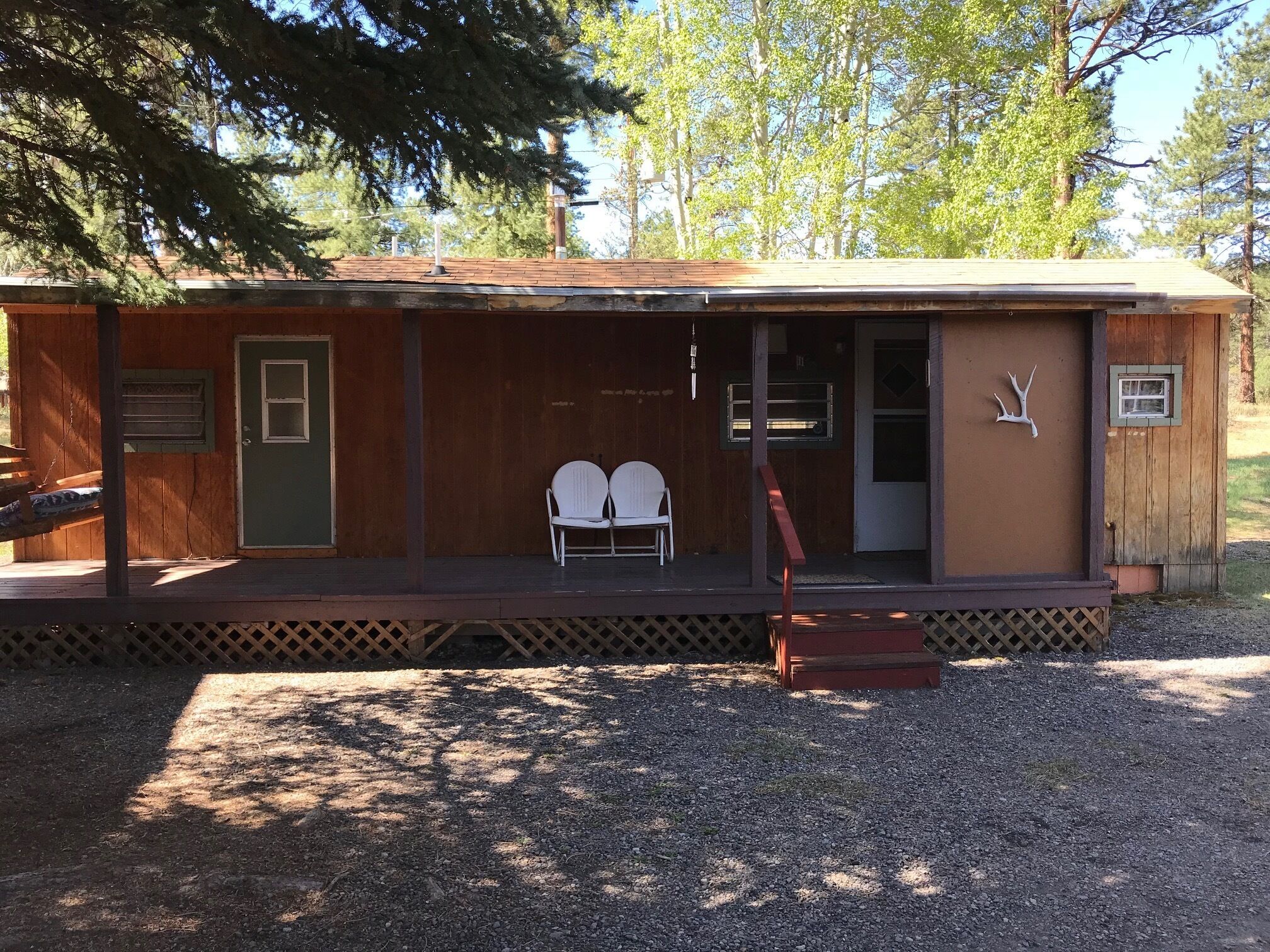 Une cabane rustique dotée d’un porche, de deux chaises blanches et d’une décoration représentant une tête de cerf.