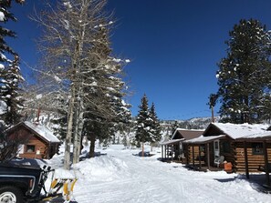 A snow-covered lodge with log cabins, a clear blue sky, and a snowmobile parked nearby. - Grandview Cabins & RV Resort (South Fork)