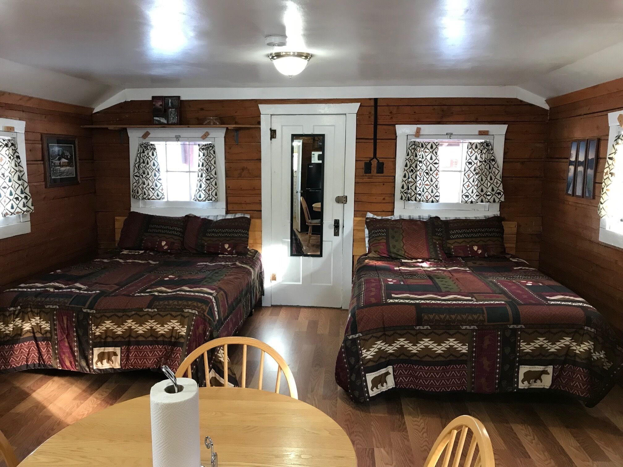 A cozy cabin room with two beds, wooden walls, and a dining area with a table and chairs.
