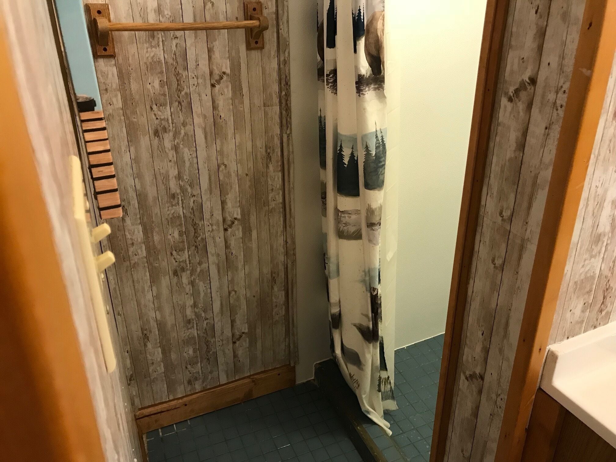 Een smalle badkamer met houten wanden, een douchegordijn met een natuurprint en een houten handdoekhouder.