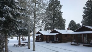 A snow-covered lodge with multiple cabins, each featuring a porch and a chimney.