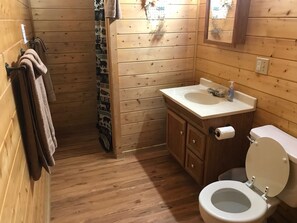 A small, wooden cabin-style bathroom with a toilet, sink, and towel rack.