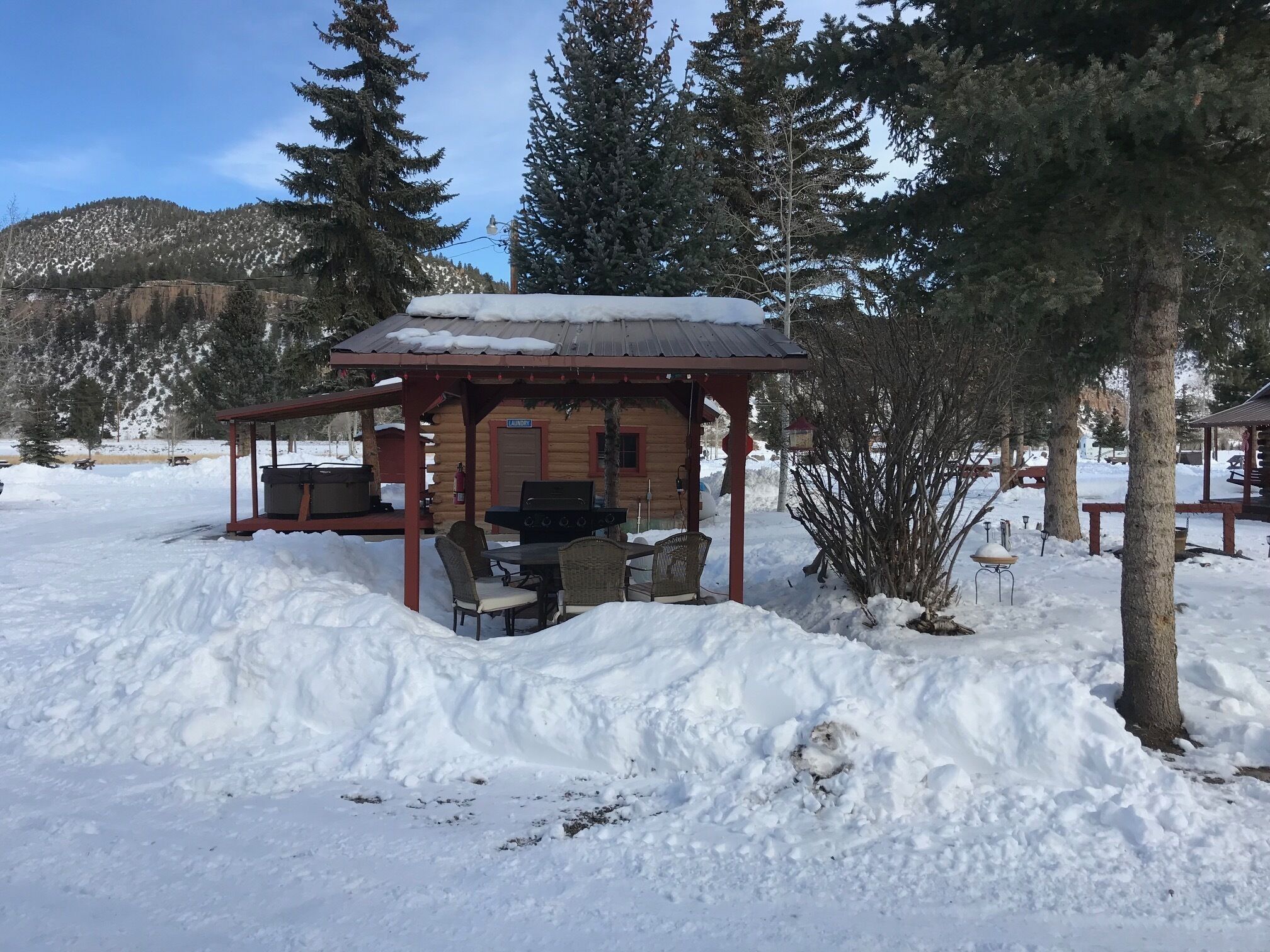 A wooden cabin with a covered patio, a barbecue grill, and a laundry area.