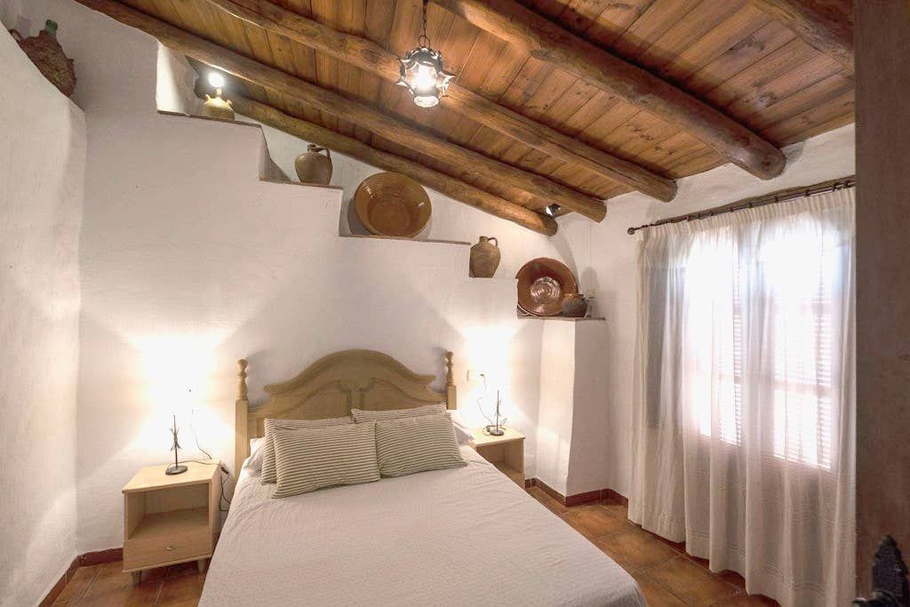 Ein Schlafzimmer mit Holzboden, einem Bett mit weißer Bettwäsche, zwei Nachttischen und einem Fenster mit Vorhängen.