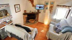 A cozy living room with a fireplace, a television mounted on the wall, and a sofa with cushions. - La Solana, your corner in the Serranía de Ronda (Benadalid)