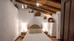 A bedroom with a wooden ceiling, a bed with a headboard, bedside tables, and wall-mounted shelves with pottery. - La Solana, your corner in the Serranía de Ronda (Benadalid)