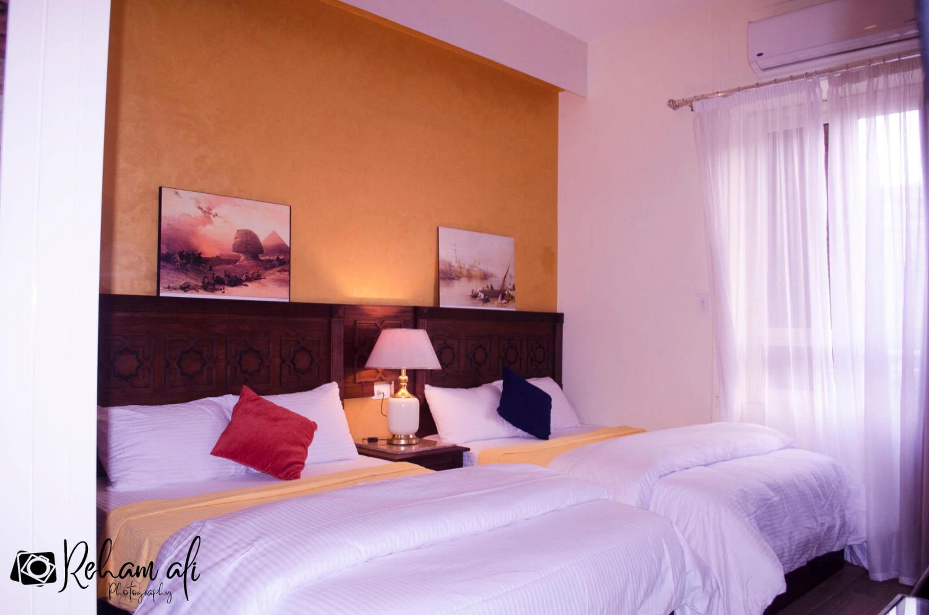 Une chambre d’hôtel avec deux lits, une tête de lit en bois, une table de chevet avec une lampe et des œuvres d’art accrochées au mur.