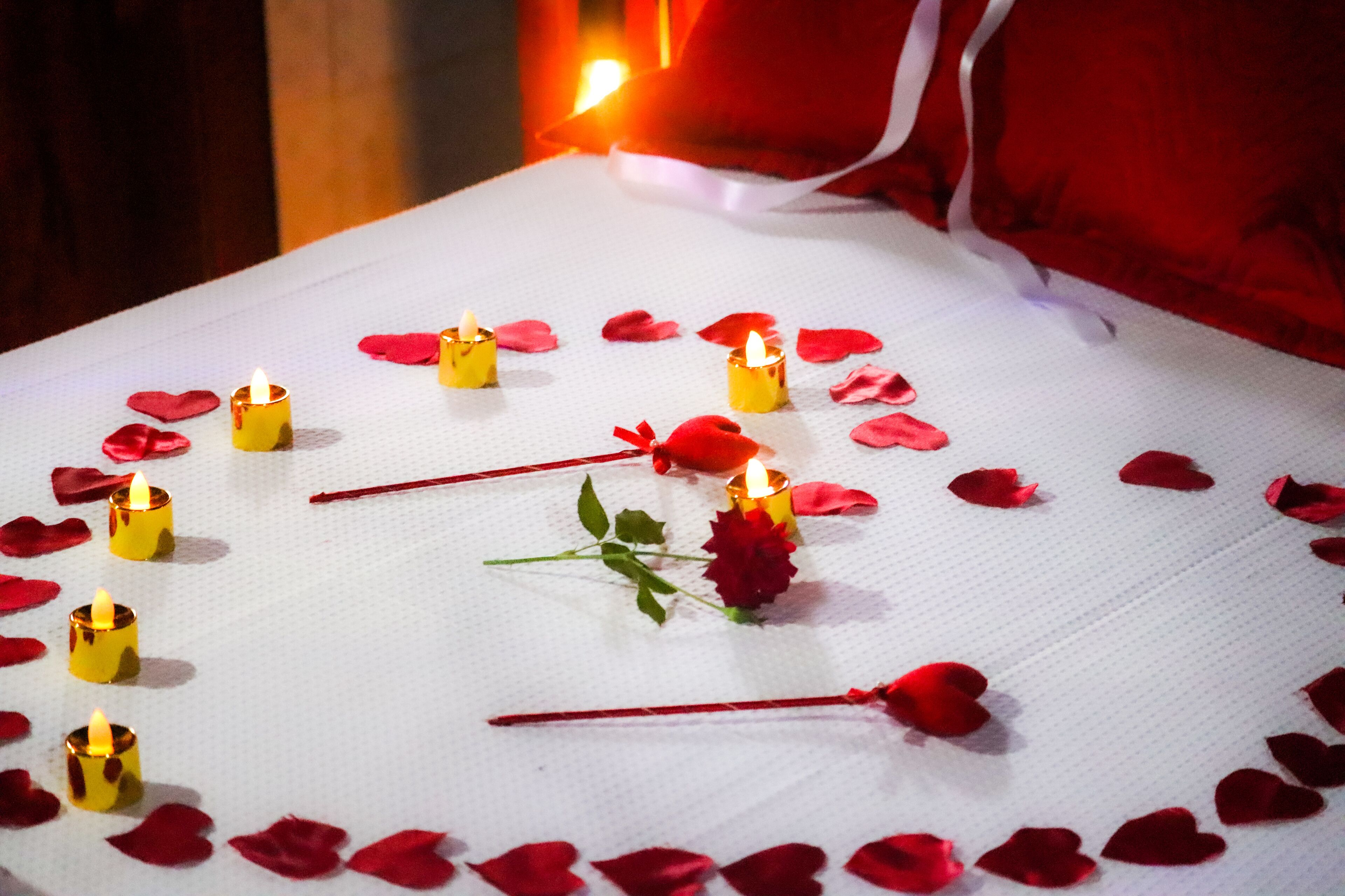 A table with candles and rose petals arranged in a heart shape.