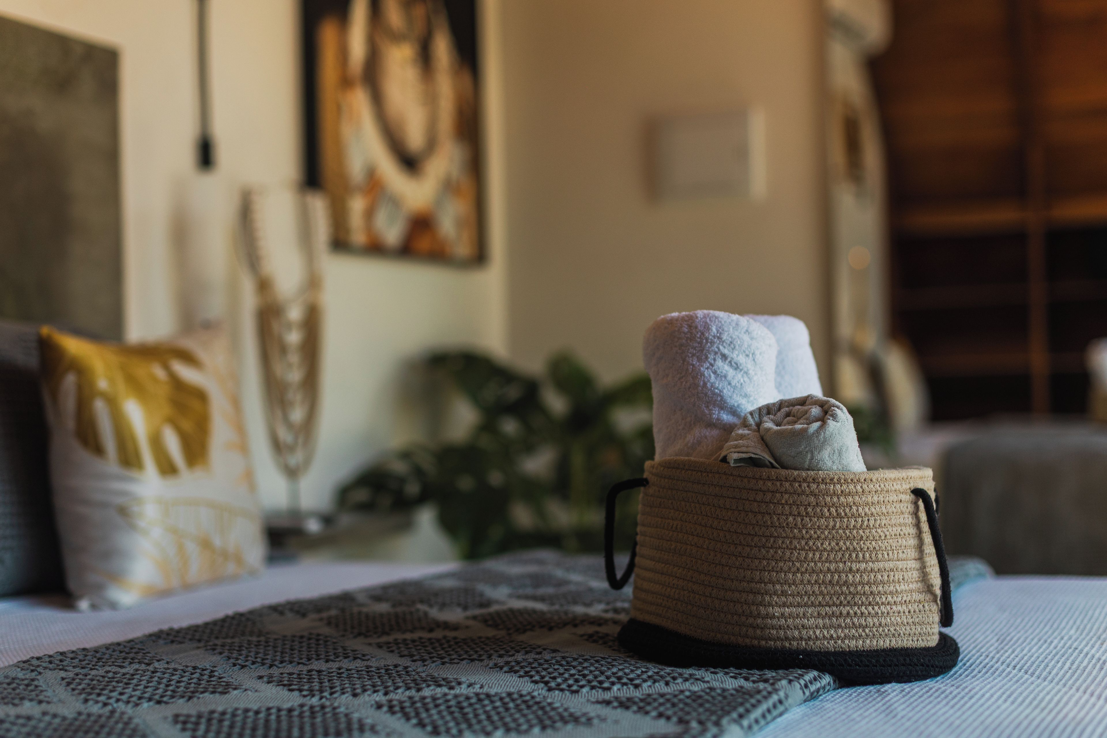 A cozy room with a woven basket containing a folded towel, a patterned rug, and a cushion on a bed.