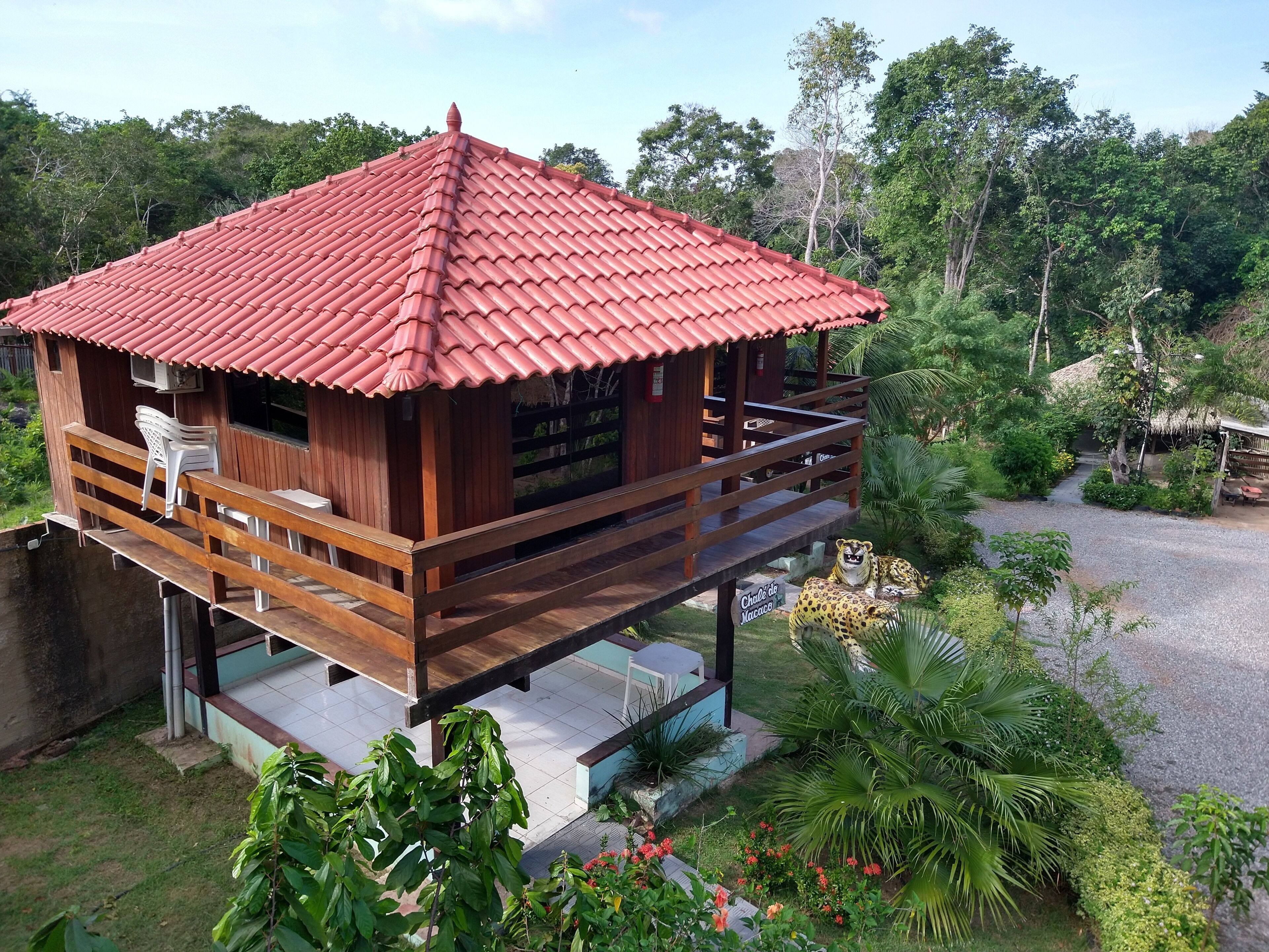 A wooden cabin with a red-tiled roof, a balcony, and a small garden area.