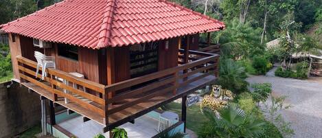 A wooden cabin with a red-tiled roof, a balcony, and a small garden area.