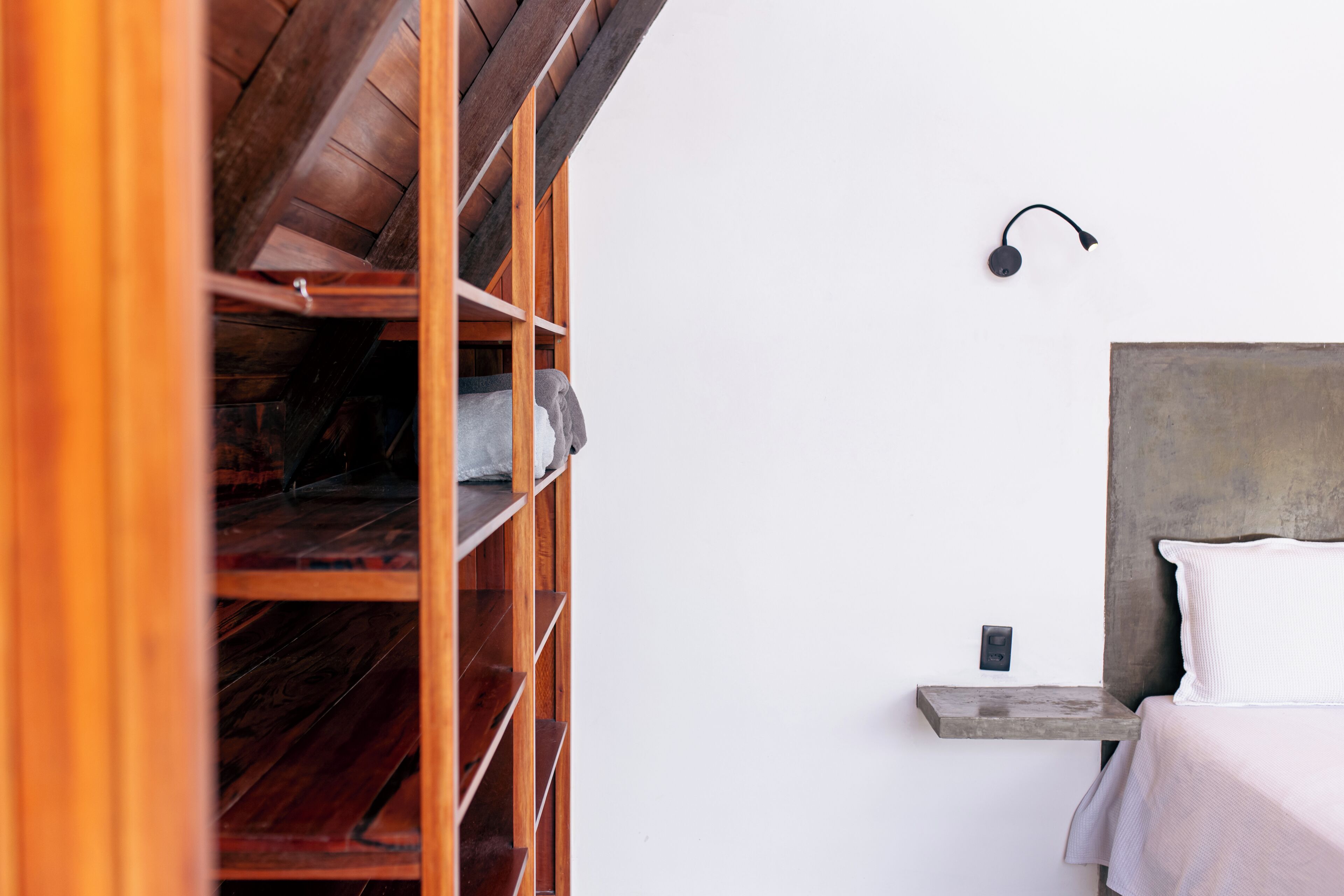 Un dormitorio con un armario de madera, una cama con cabecero blanco y una lámpara fijada a la pared.