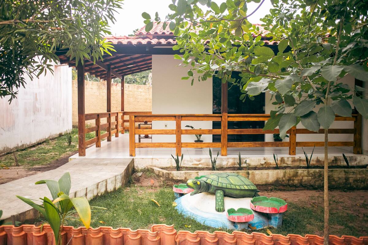 A covered outdoor area with a wooden deck, a small garden with a turtle sculpture, and a building with a tiled roof.