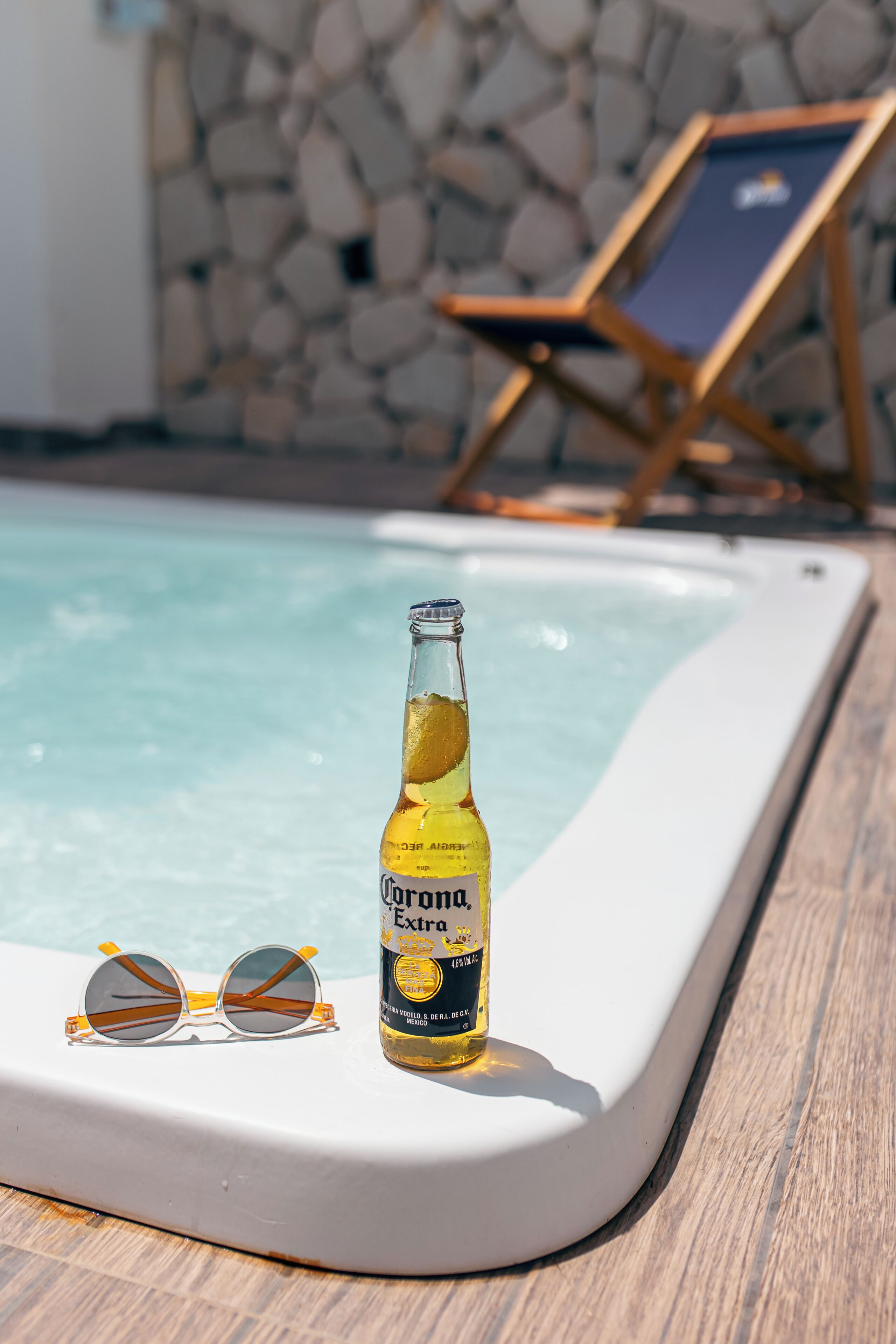 A bottle of Corona beer and sunglasses on a poolside deck.