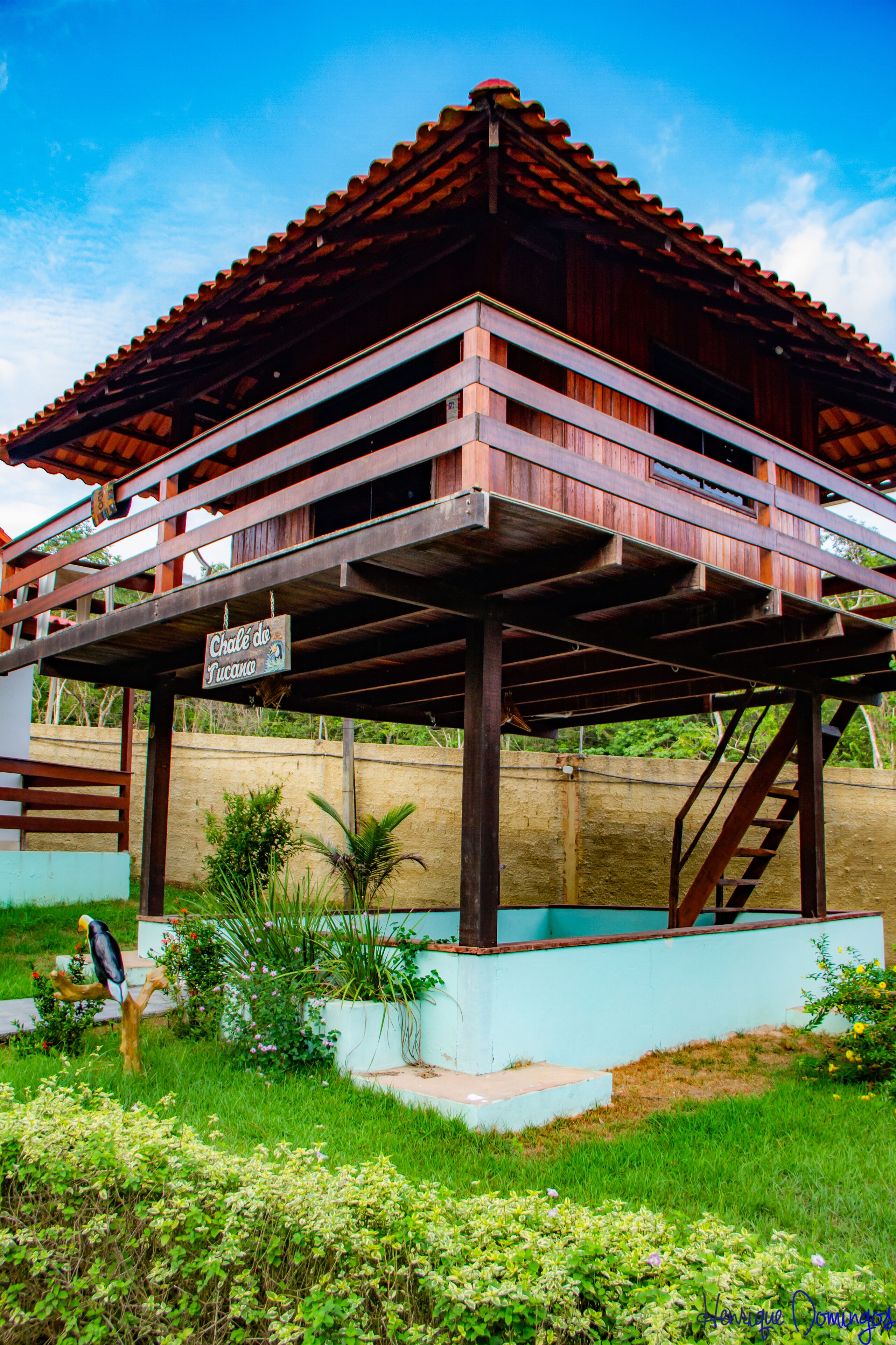 A two-story wooden structure with a tiled roof, a sign reading "Chalet da Lua," and a staircase leading to the upper level.