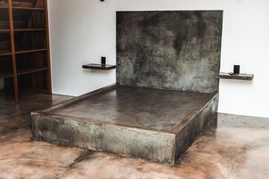Una habitación minimalista con una cama grande, estanterías de madera y suelo de hormigón.