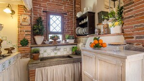 A kitchen with a brick wall, a window, and various kitchen items like plants, jars, and a fruit bowl. - ROSYABATE COTTAGE with Private Garden and views between Lucca and Pistoia (Uzzano)