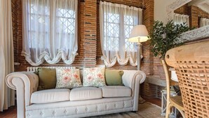 A cozy room with a white upholstered sofa, a woven rug, and a wicker chair. - ROSYABATE COTTAGE with Private Garden and views between Lucca and Pistoia (Uzzano)