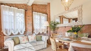 A cozy dining area with a white table set for two, a white sofa with floral cushions, and a brick wall backdrop. - ROSYABATE COTTAGE with Private Garden and views between Lucca and Pistoia (Uzzano)
