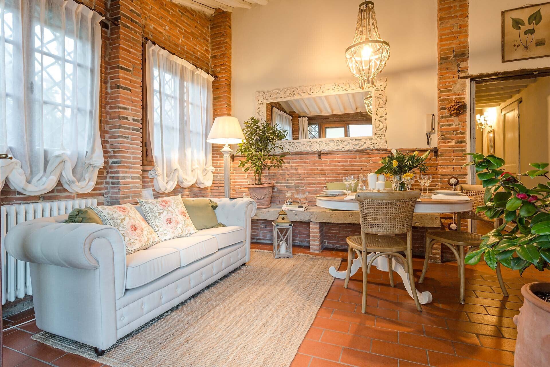A cozy room with a white sofa, a dining table with chairs, a mirror, and a hanging light fixture.