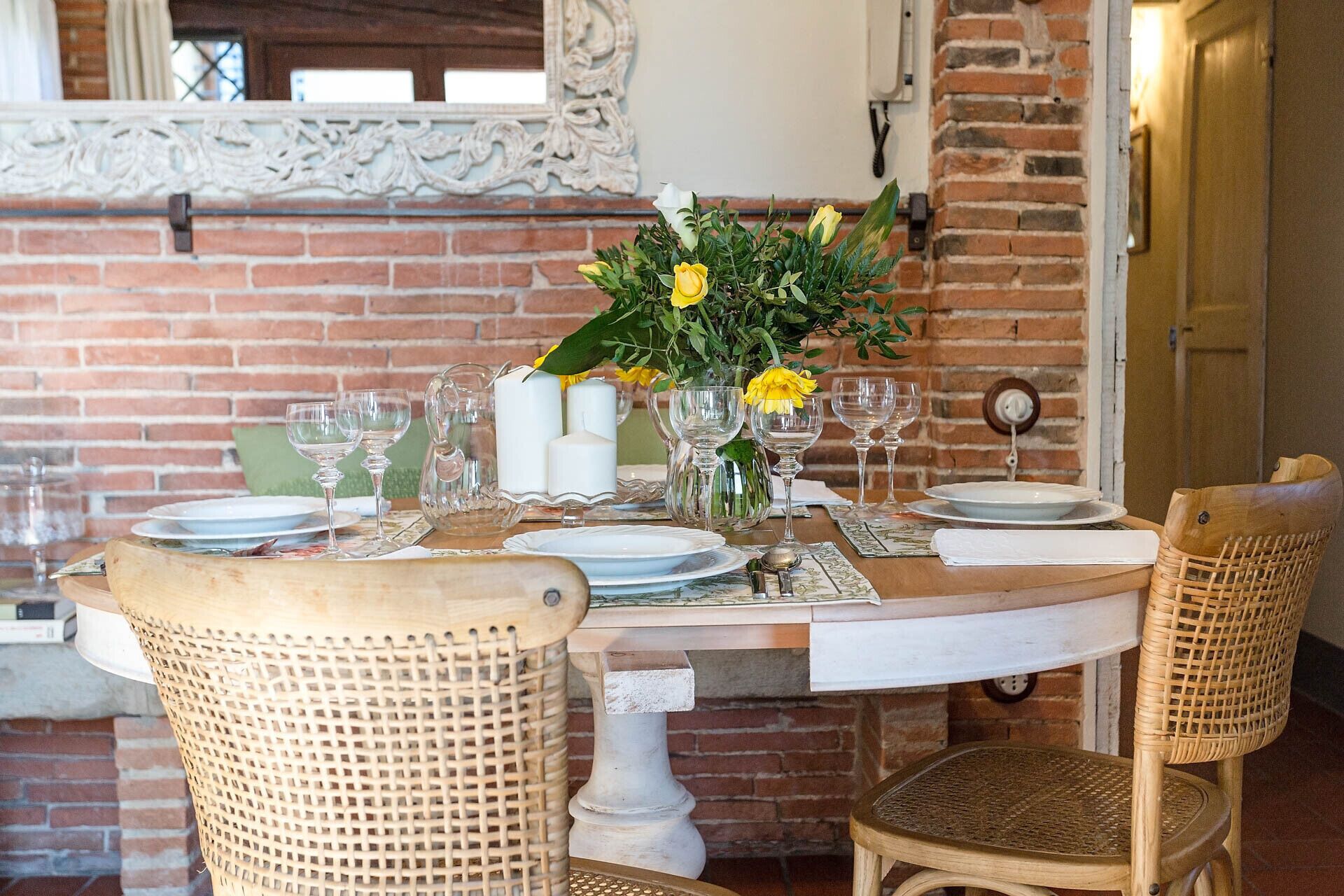A dining table set with white plates, clear glasses, and a centerpiece of yellow flowers.