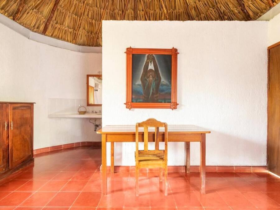 A room with a wooden table and chair, a framed picture on the wall, and a tiled floor.