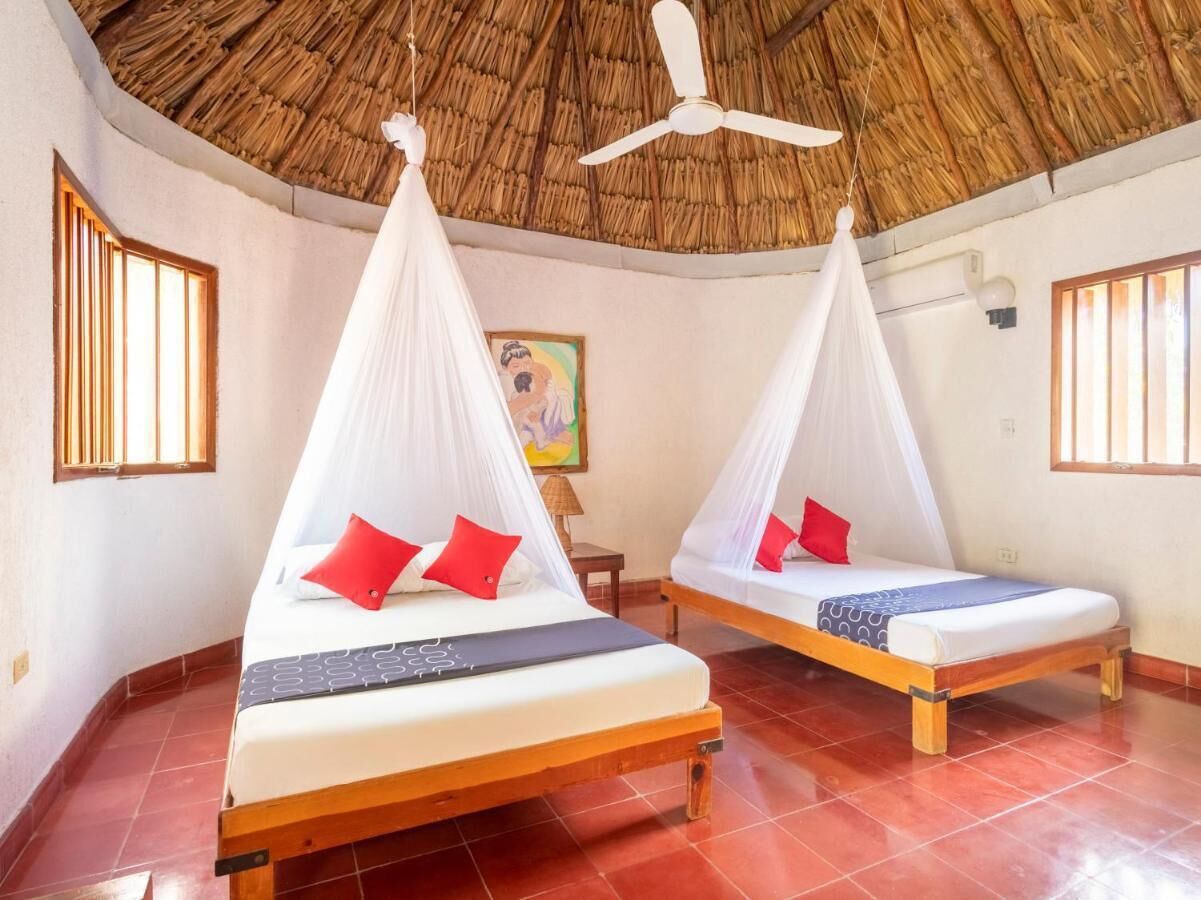 Two beds with mosquito nets, a ceiling fan, and a painting on the wall.