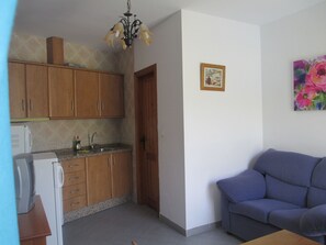 A kitchen with wooden cabinets, a built-in oven, and a sink. There is a blue sofa in the living area and a painting on the wall.