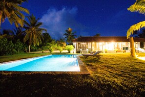 A swimming pool with a clear blue water surface, surrounded by a well-maintained lawn and palm trees. - Ardeen Villa (Kahandamodara)