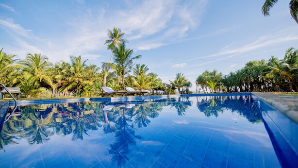 A clear blue swimming pool with reflections of palm trees and a clear sky. - Ardeen Villa (Kahandamodara)