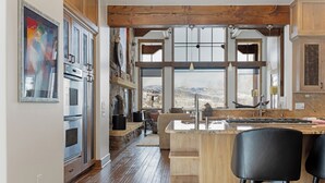 A modern kitchen with a stone backsplash, wooden beams, and a large window overlooking a mountainous landscape.