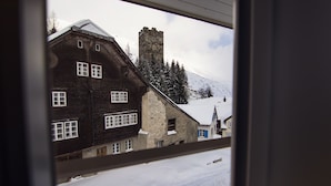 En traditionel schweizisk chalet med en stensøjle, flere vinduer og et sneklædt landskab, der ses gennem et vindue.
