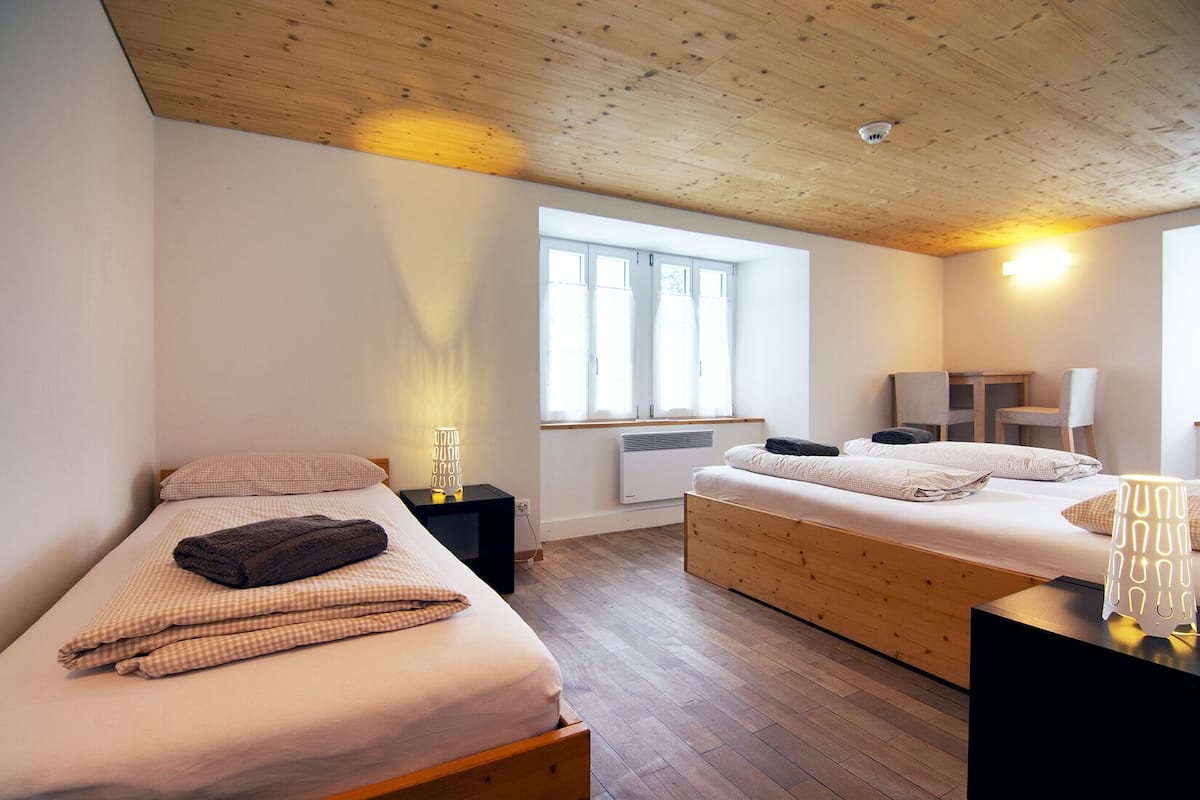 A modern bedroom with two beds, a wooden ceiling, a window, and a desk with a chair.