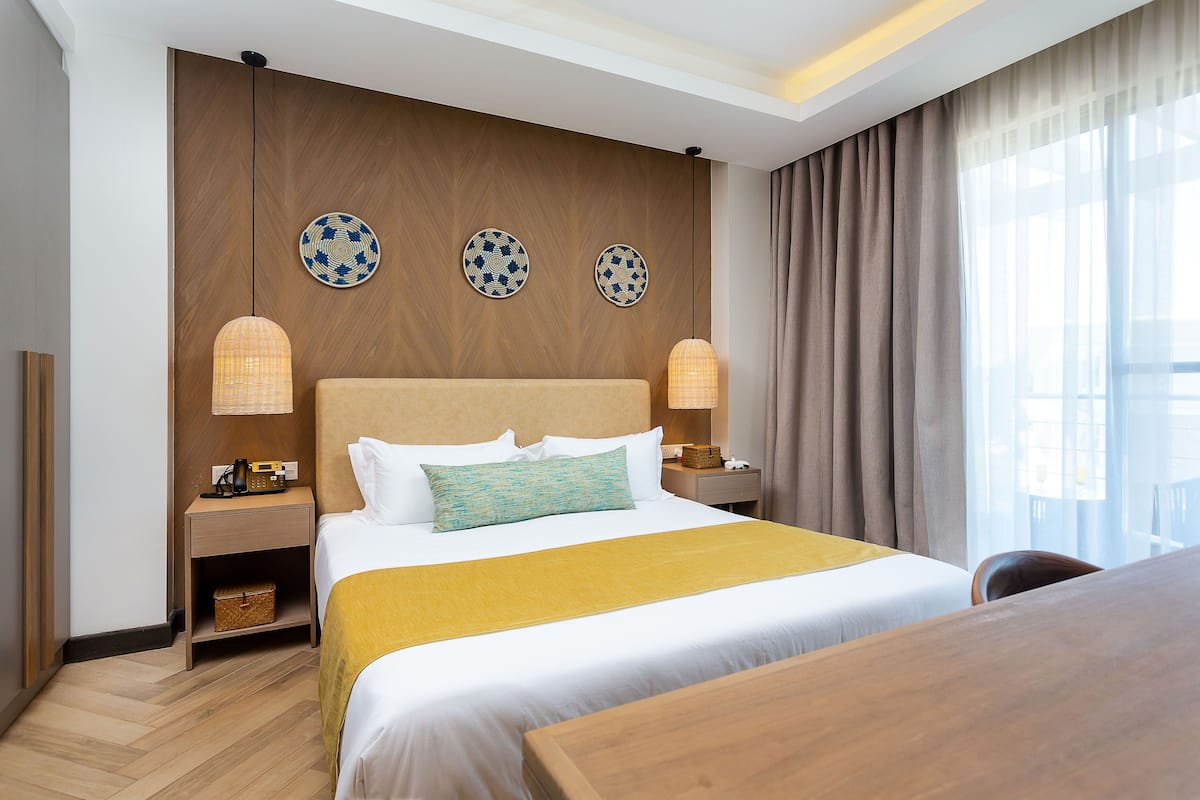 A hotel room with a large bed, bedside tables, a desk, and a view of the city through the window.