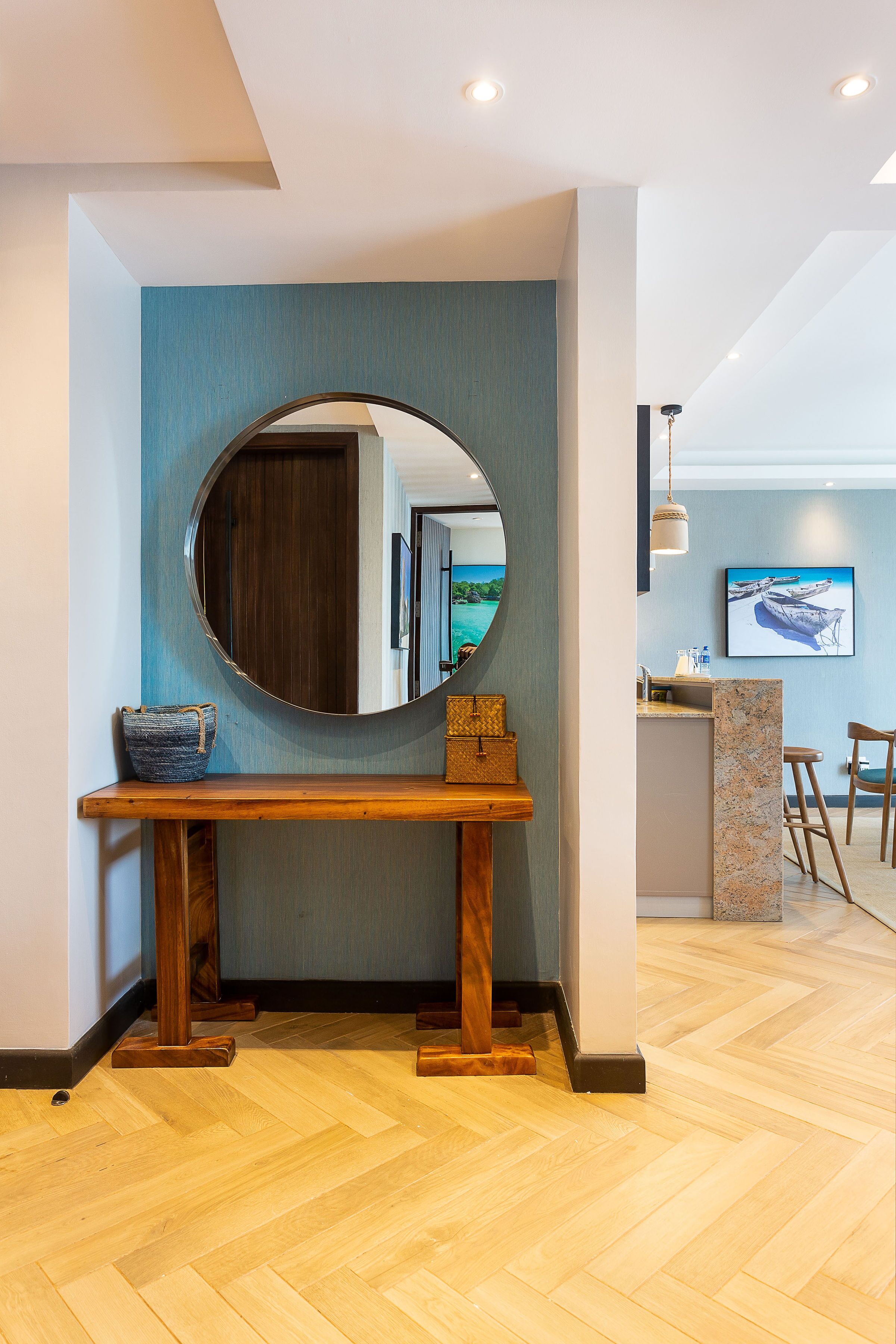 Un interior moderno con una consola de madera, un espejo redondo y vistas a una zona de cocina.