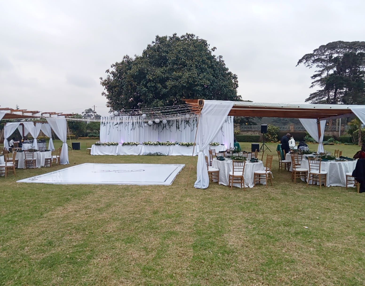 Un lieu de réception en plein air, idéal pour un mariage, avec une grande piste de danse, des auvents blancs et des tables dressées pour les invités.