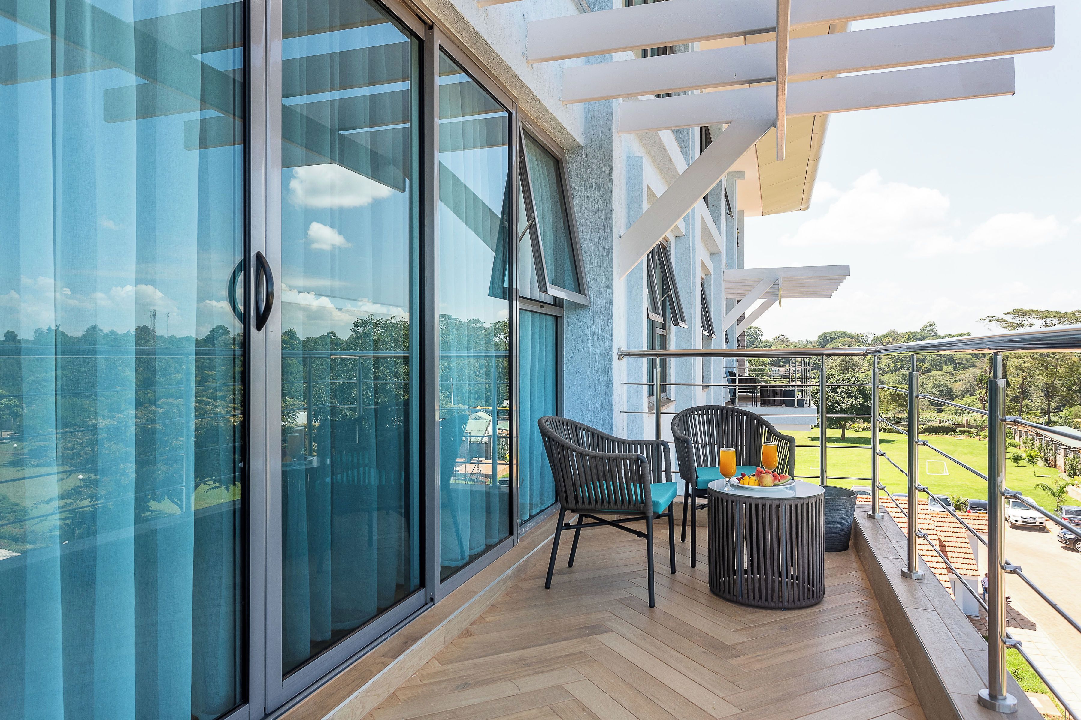 Een balkon met uitzicht op een groen landschap, een tafel met stoelen en een glazen deur.