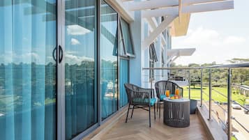 Een balkon met uitzicht op een groen landschap, een tafel met stoelen en een glazen deur.
